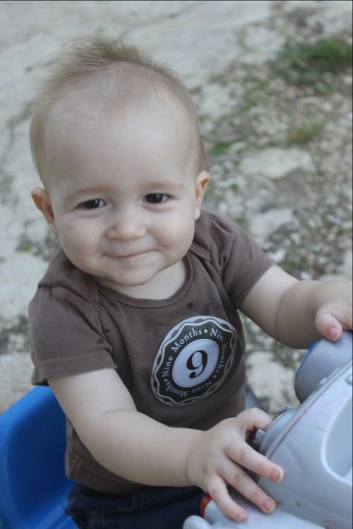 Josiah, 9 months old, sitting on a tricycle